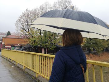 Woman with umbrella standing by railing on street