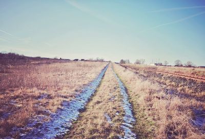 Dirt road amidst field against sky