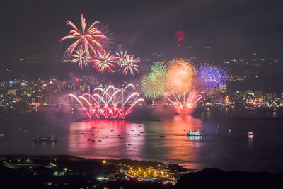 Firework display over illuminated city against sky at night