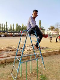 Full length of young man sitting on play equipment outdoors