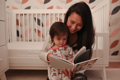 Smiling mother reading book to daughter at home