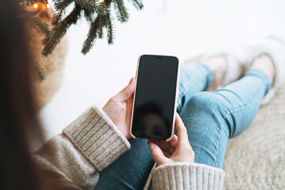 Young woman using mobile smartphone in room with christmas tree at home