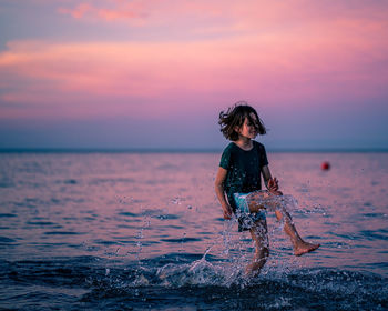 Woman in sea against sky during sunset