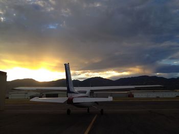 Airplane on airport runway against sky during sunset