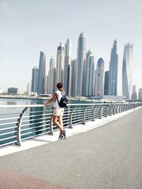 Rear view of woman with arms outstretched against cityscape in dubai