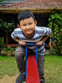 Portrait of smiling boy sitting on seesaw in playground