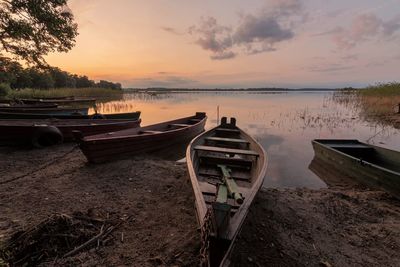 Boats moored on shore against sky during sunset