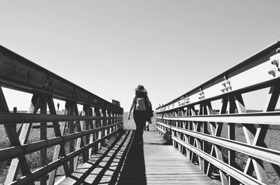 Rear view of woman standing on footbridge against clear sky