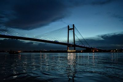 Suspension bridge over river against sky at night