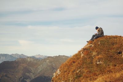 Man sitting on rock looking at mountains against sky