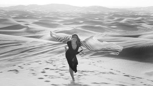 Full length of smiling woman standing on sand in desert
