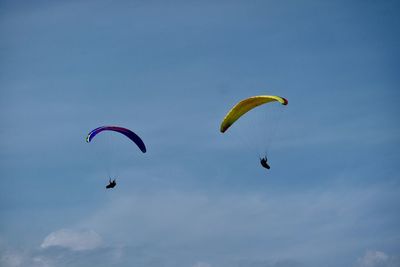 Low angle view of people paragliding against sky