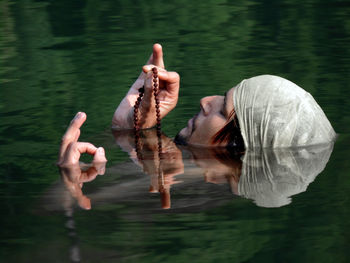 Young man holding prayer beads while swimming in lake