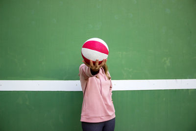 Young woman holding basketball against wall