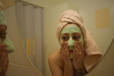 Young woman analyzing facial mask in mirror