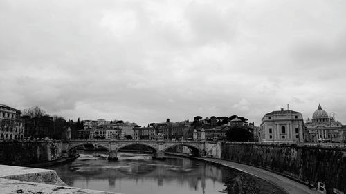 Bridge over river by buildings against sky