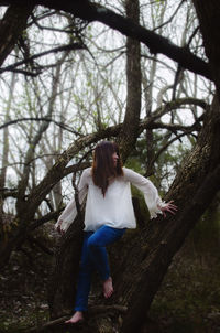 Woman leaning amidst tree trunk in forest