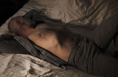 Adult man in open shirt and jeans lying on bed