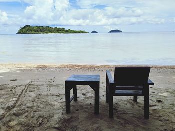 Empty chairs and table on beach against sky
