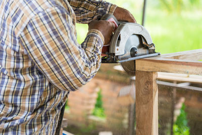 Midsection of man cutting wood with circular saw
