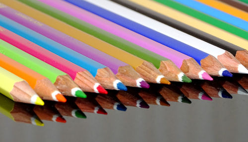 Close-up of colored pencils on glass table with reflection