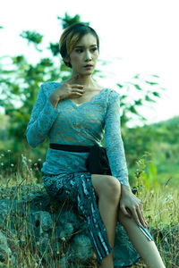 Young woman looking away while sitting on field