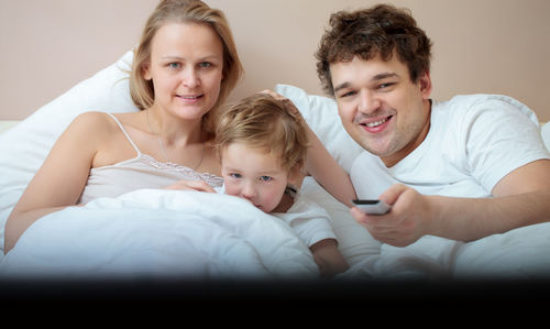 Happy family watching tv while resting on bed