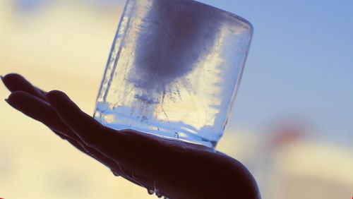 Close-up of hand holding water against sky