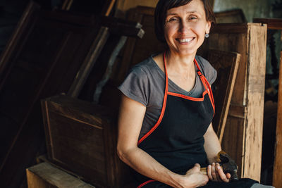 Happy female carpenter with hammer in workshop smiling at camera