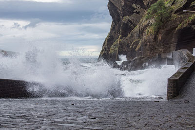 Waves splashing on rocks at shore against sky