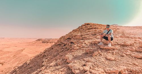 Man on rock in desert against sky