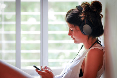 Woman listening music while sitting on window sill