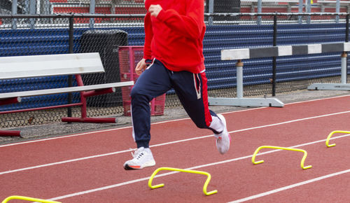A high school track runner is running the wicket drill by running over small hurdles on a track.
