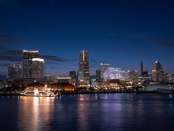 Illuminated buildings by river against sky at night