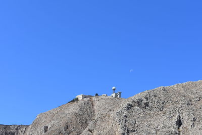 Low angle view of people on rock against blue sky