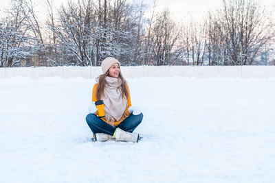 Portrait of happy young woman with ice skates sitting on the snow and holding mug with coffee