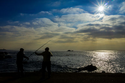 Silhouette people fishing in sea against sky