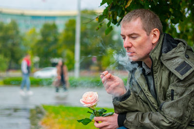 Smoking man with a rose sits in the park thinking
