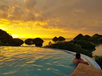 Man swimming in infinity pool by sea against sky during sunset