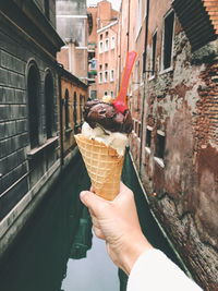 Cropped image of hand holding ice cream cone against  buildings  in venice