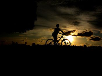 Silhouette man riding bicycle against sky during sunset