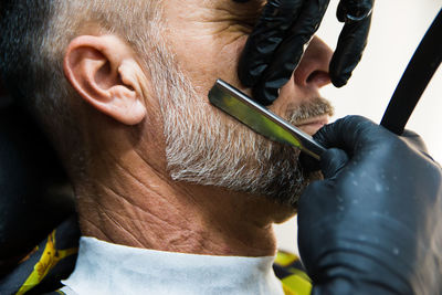 Cropped hands of barber cutting beard of man at salon