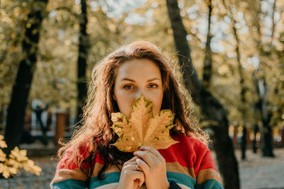 Portrait of young woman holding plant against tree