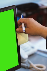 Cropped hand of business person sticking adhesive note on computer monitor in office