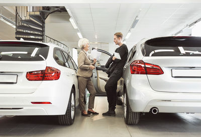 Full length of senior saleswoman talking to male customer at car dealership