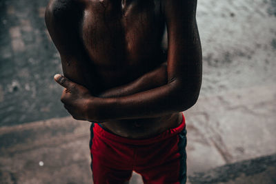 Midsection of shirtless man standing against wall