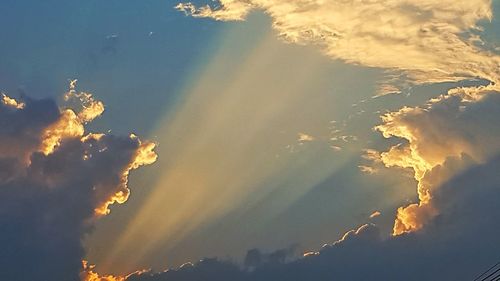 Low angle view of sunlight streaming through clouds during sunset