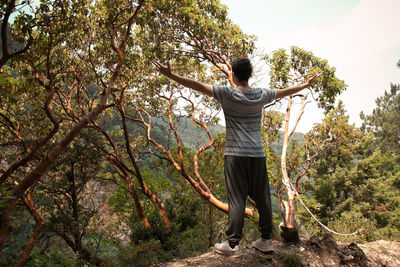 Rear view of man standing with arms outstretched on rock