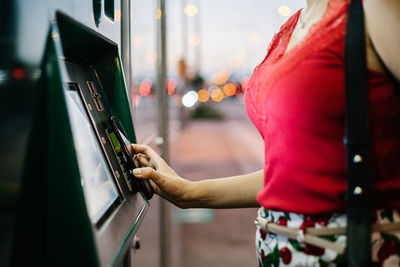 Side view of cropped unrecognizable female passenger buying ticket for public transport on vending machine