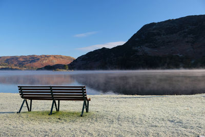 Empty bench by lake against sky